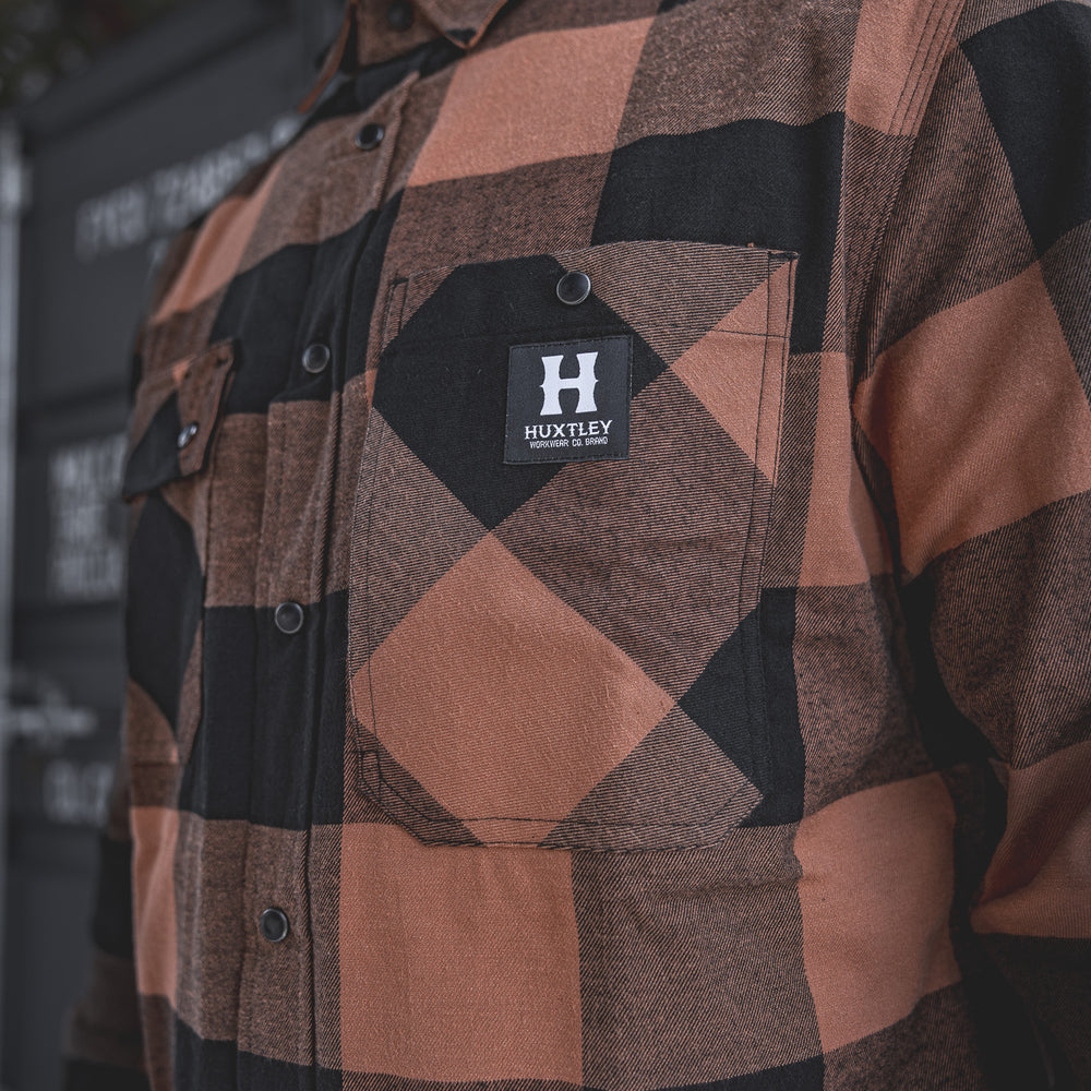 
                  
                    Close-up of the Huxtley HD-57 Flex Flannel in Whiskey/Black, showcasing the signature chest pocket with branded snap and bold buffalo check pattern. Built tough with attention to every detail.
                  
                