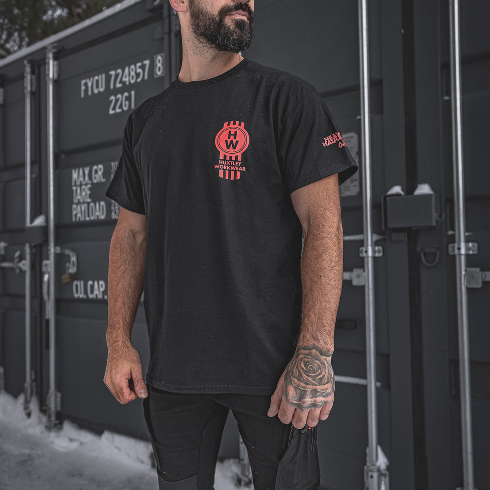 
                  
                    Model wearing the Huxtley Heavy Haulers Club tee in black with bold red chest print. 
                  
                