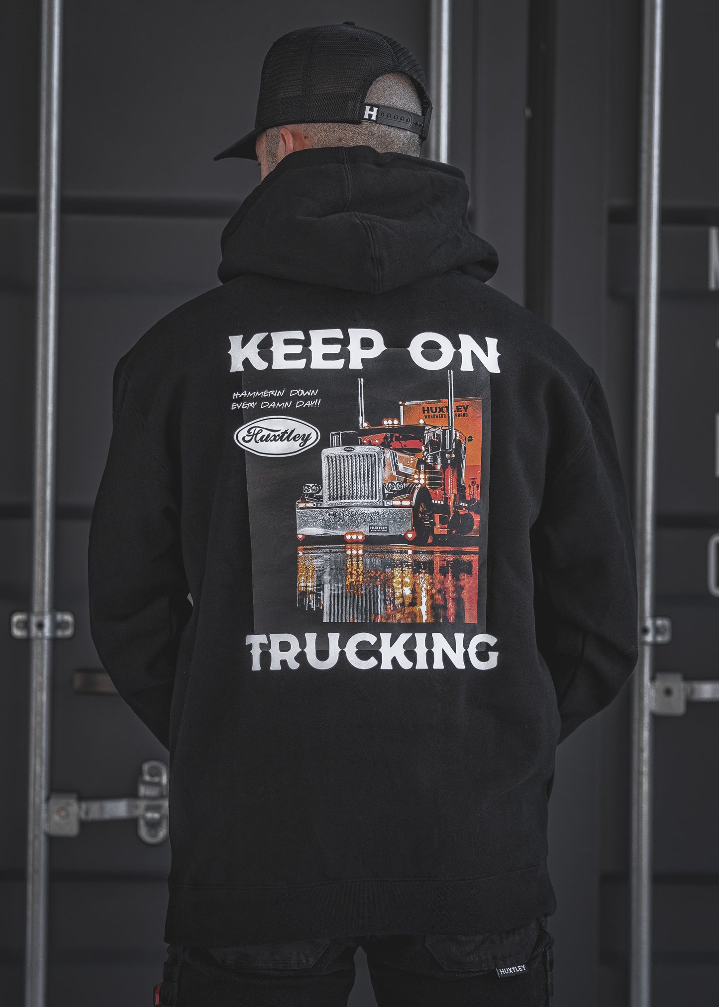 Back view of the Huxtley Keep On Trucking hoodie in black. Featuring a bold semi-truck print and “Hammerin’ Down Every Damn Day!!” motto—made for long hauls and cold yards.