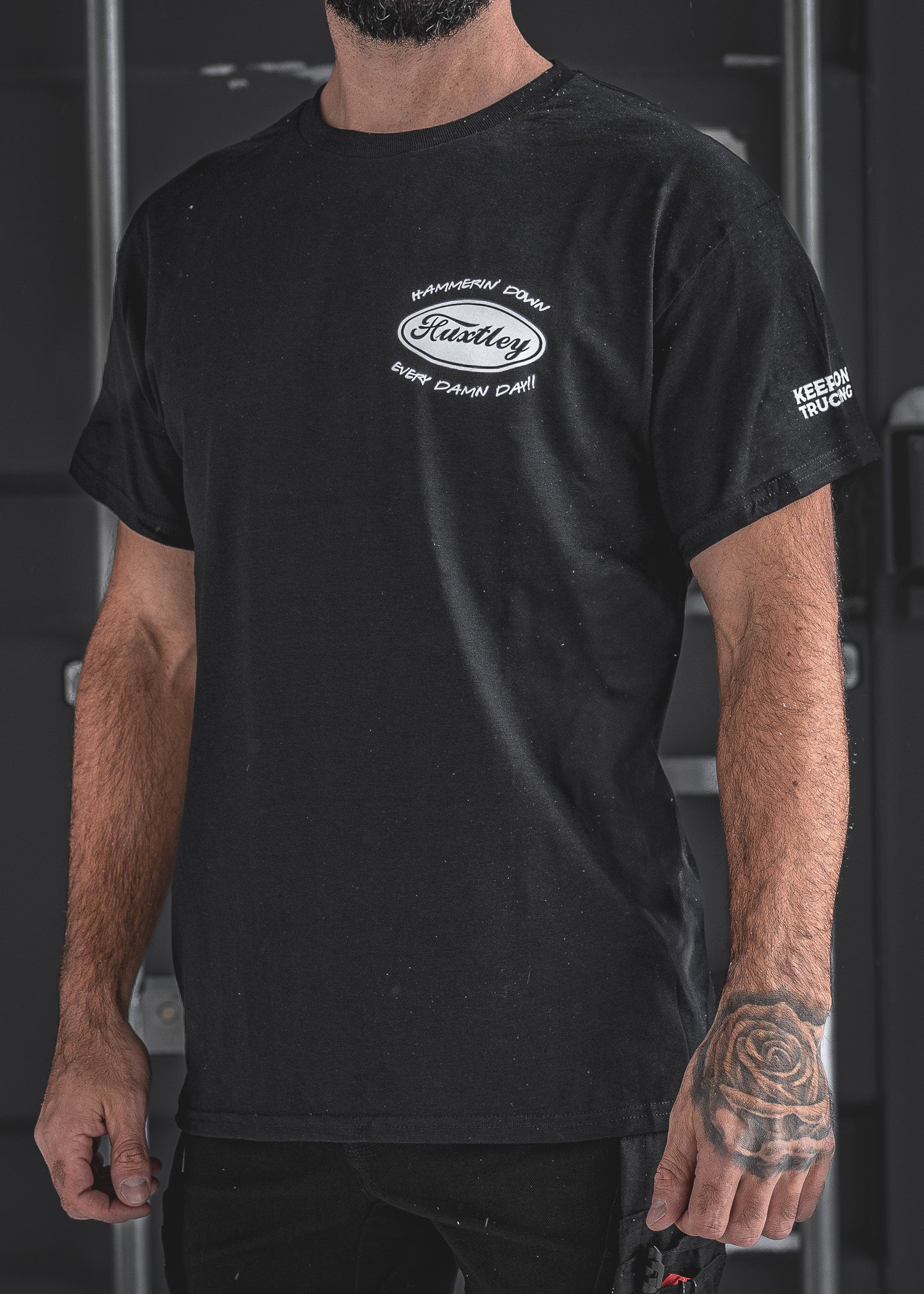 Front view of the Huxtley Keep On Trucking Tee in black, featuring the “Hammerin’ Down Every Damn Day!” chest logo and sleeve print. A bold statement for those who don’t take their foot off the gas.