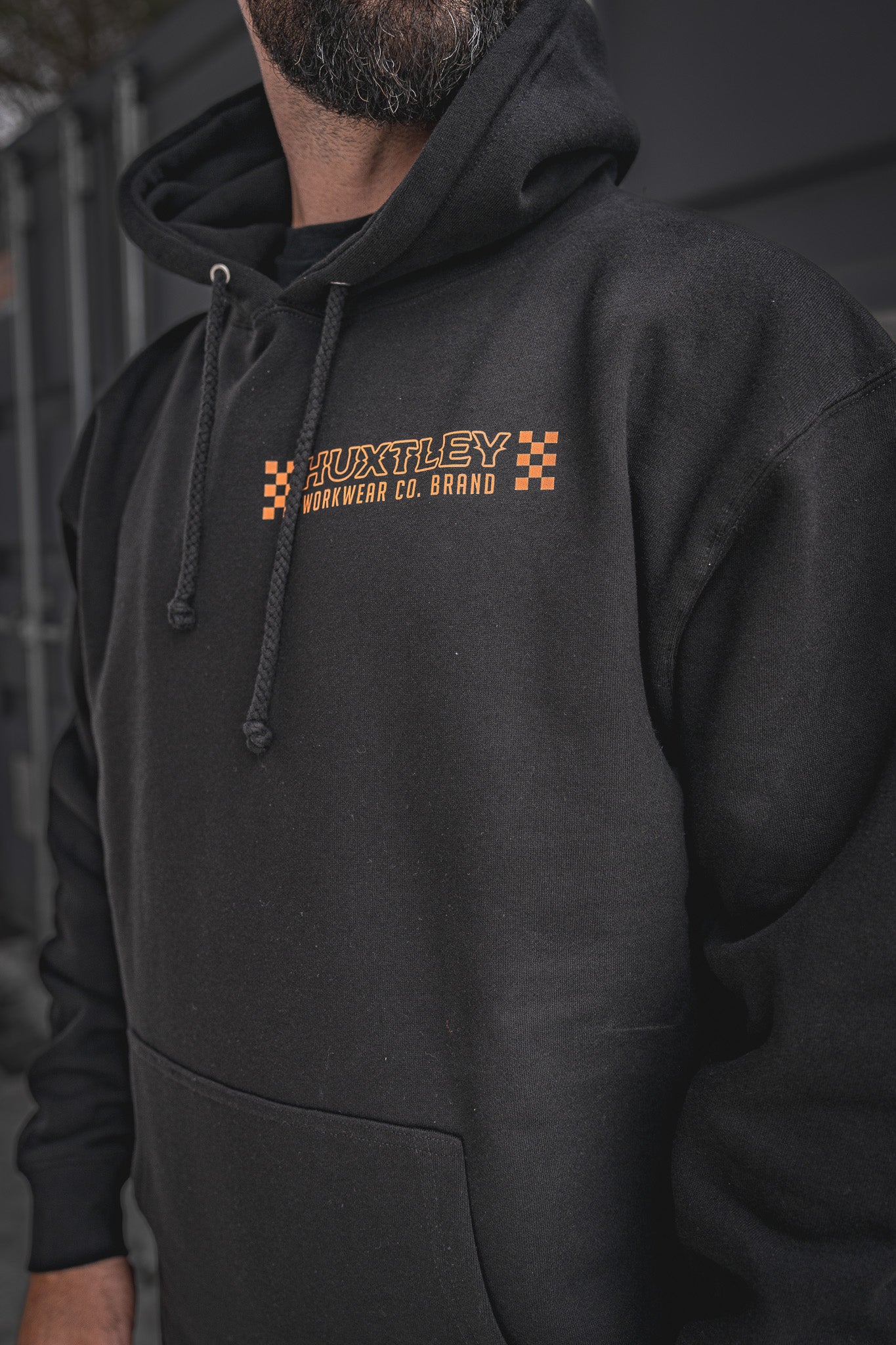 
                  
                    Detailed view of the Huxtley Work Hard Have Fun Hoodie, spotlighting the orange checkerboard chest logo. Built for the trades, styled for the street—this one’s all about hard work and good times.
                  
                