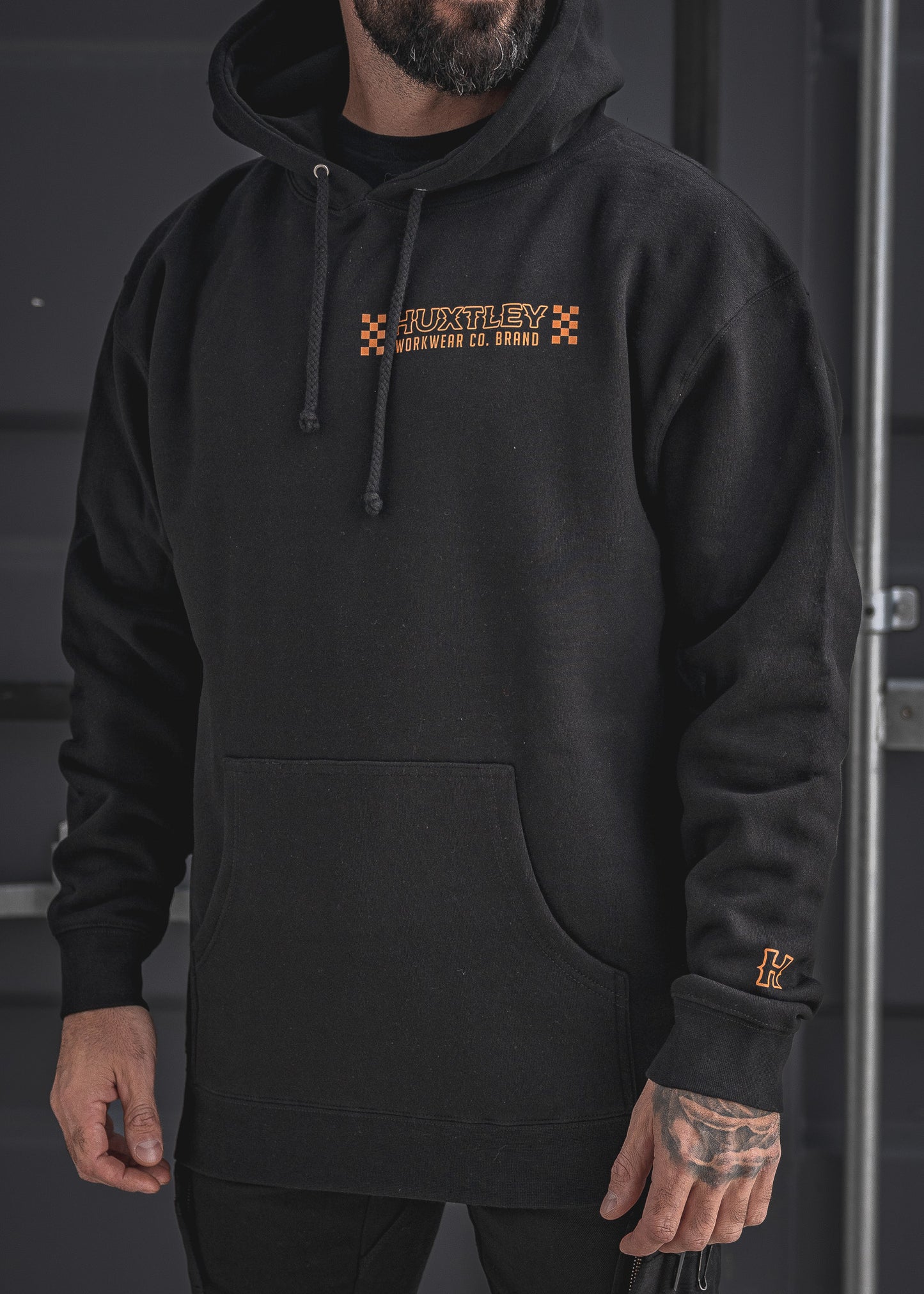 Stay sharp in the Huxtley Work Hard Have Fun Hoodie. This clean front view shows off the orange checkerboard Huxtley Workwear Co. logo and embroidered sleeve “H” – perfect blend of grit and style on the jobsite.