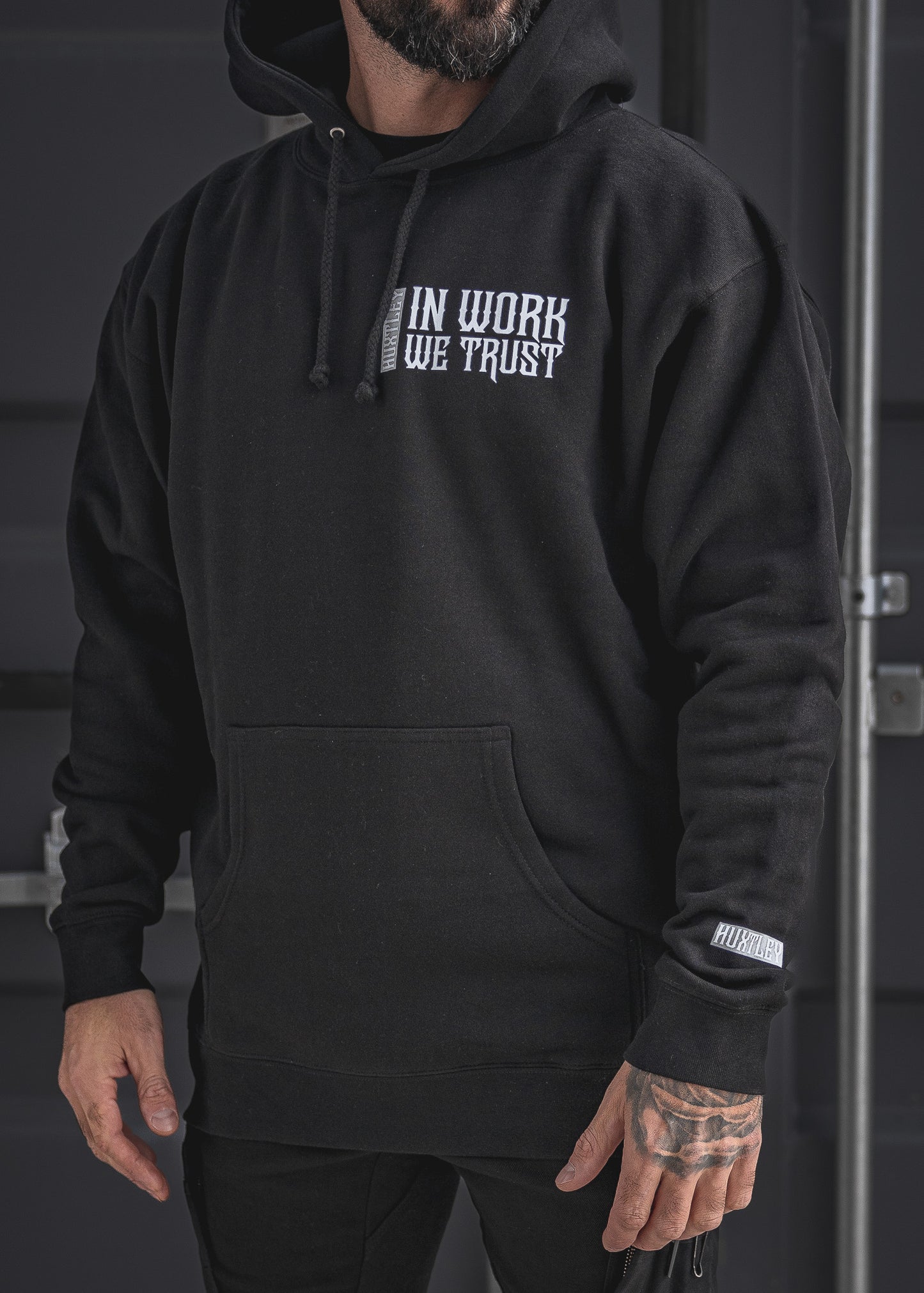 Front view of the In Work We Trust Hoodie in black, featuring bold white chest lettering and a branded cuff tag. Built for the grind, made for haulers.