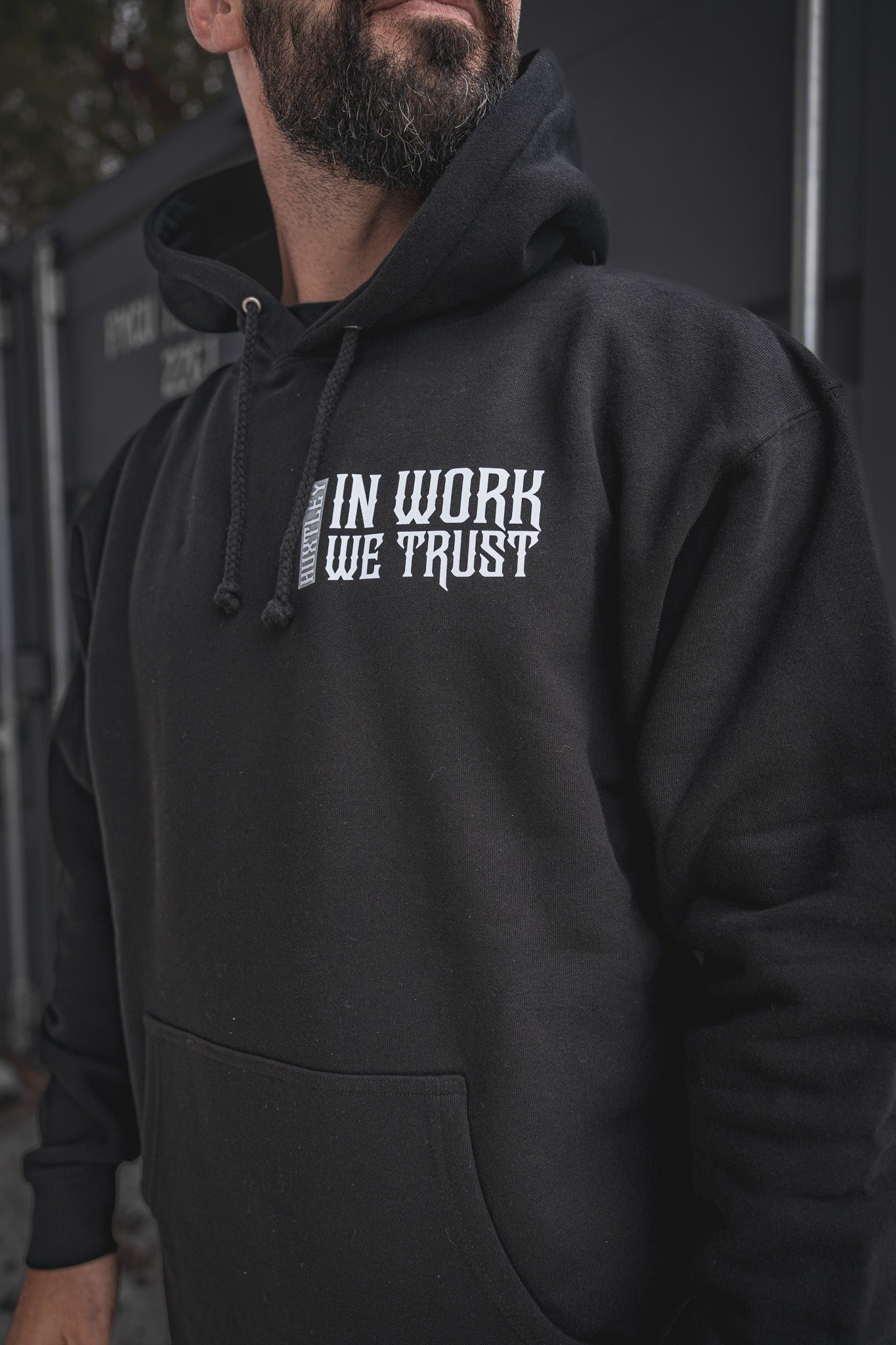 
                  
                    Close-up of the In Work We Trust Hoodie in black featuring bold gothic-style white chest print and HUXTLEY drawcord branding. For the ones who live to hustle.
                  
                