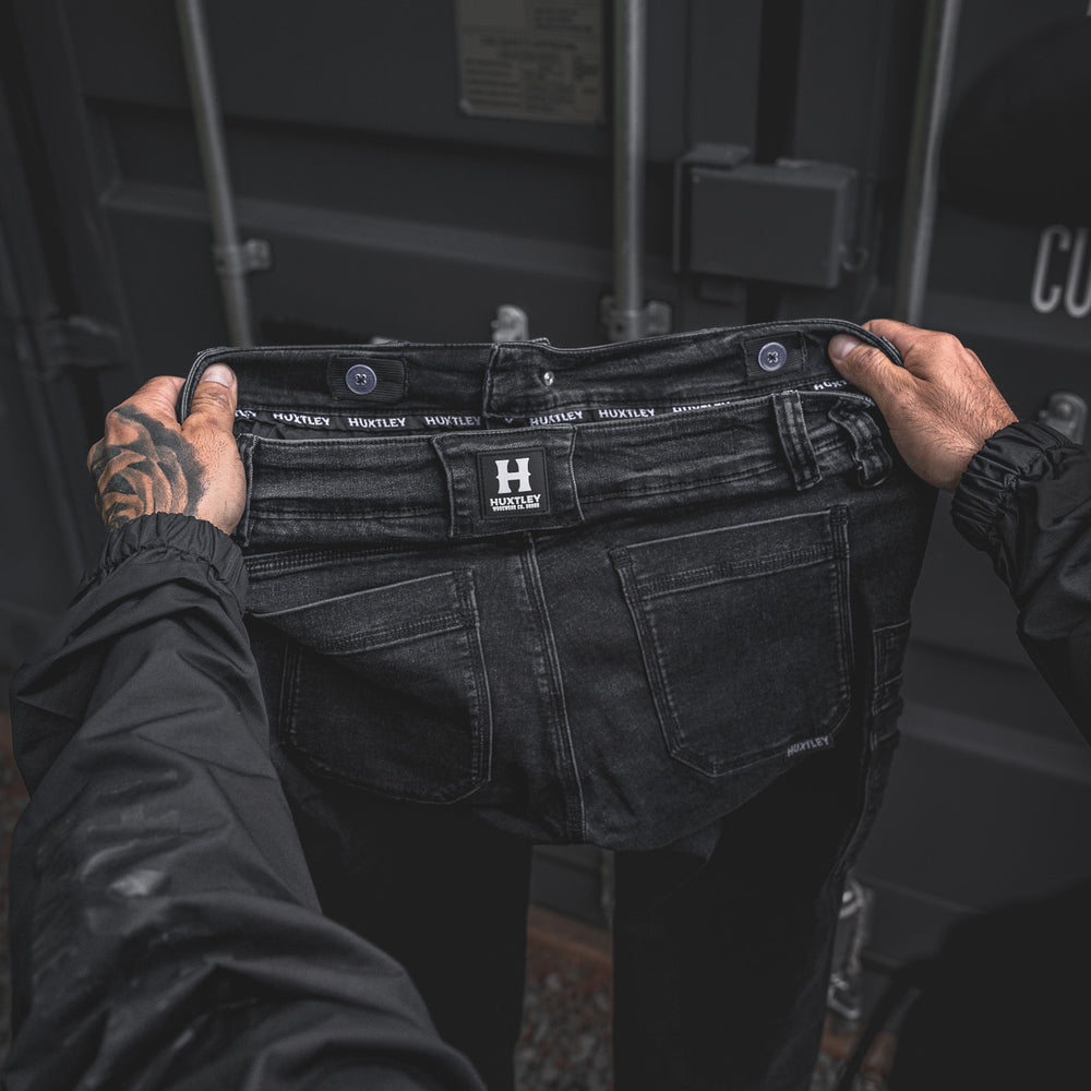 
                  
                    Close-up of the back waistband on the RX-1 Relaxed Work Jeans in Stonewashed Black, featuring the signature HUXTLEY branding and durable belt loops. Built to move, built to last.
                  
                