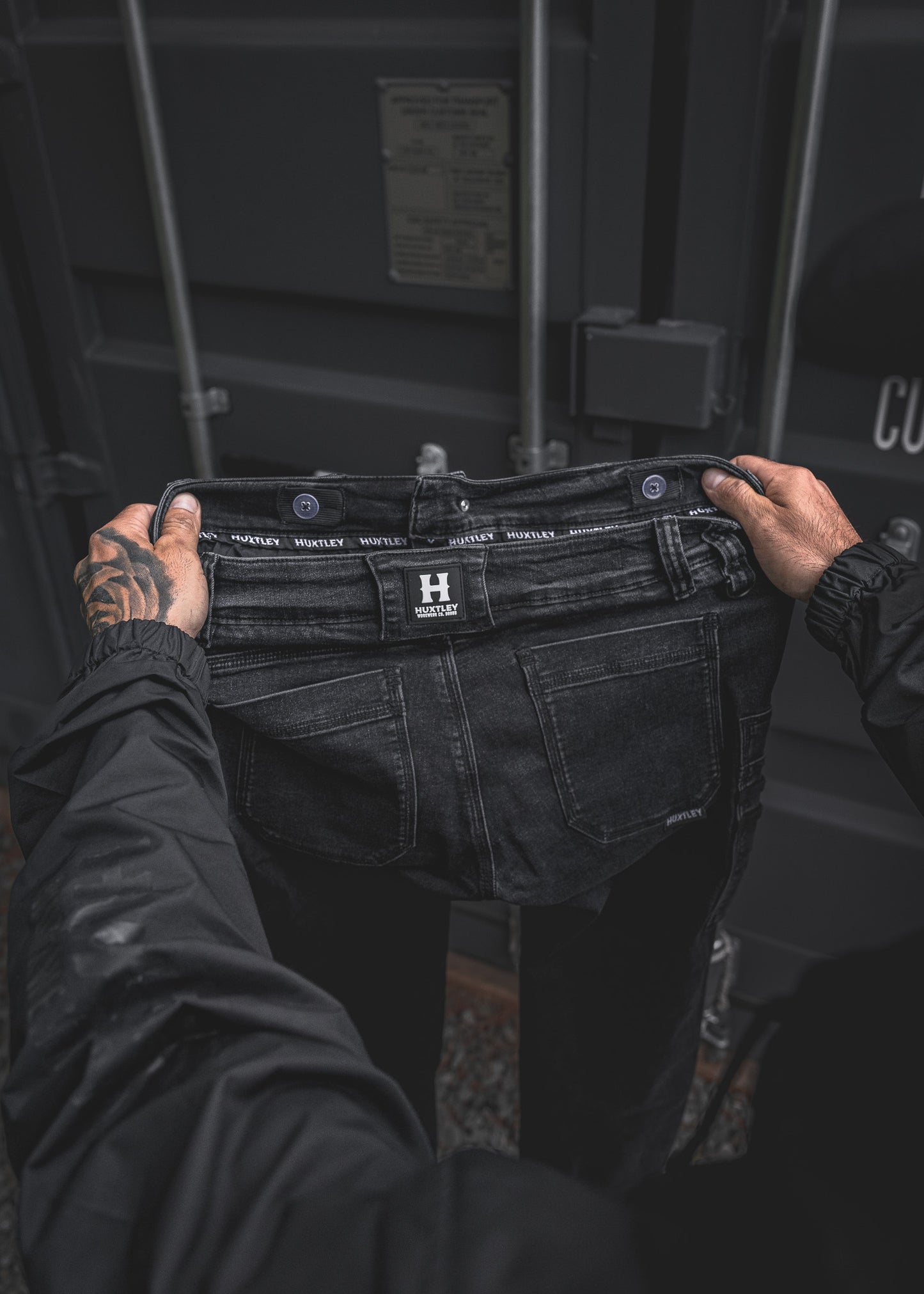 
                  
                    Close-up of the back waistband on the RX-1 Relaxed Work Jeans in Stonewashed Black, featuring the signature HUXTLEY branding and durable belt loops. Built to move, built to last.
                  
                