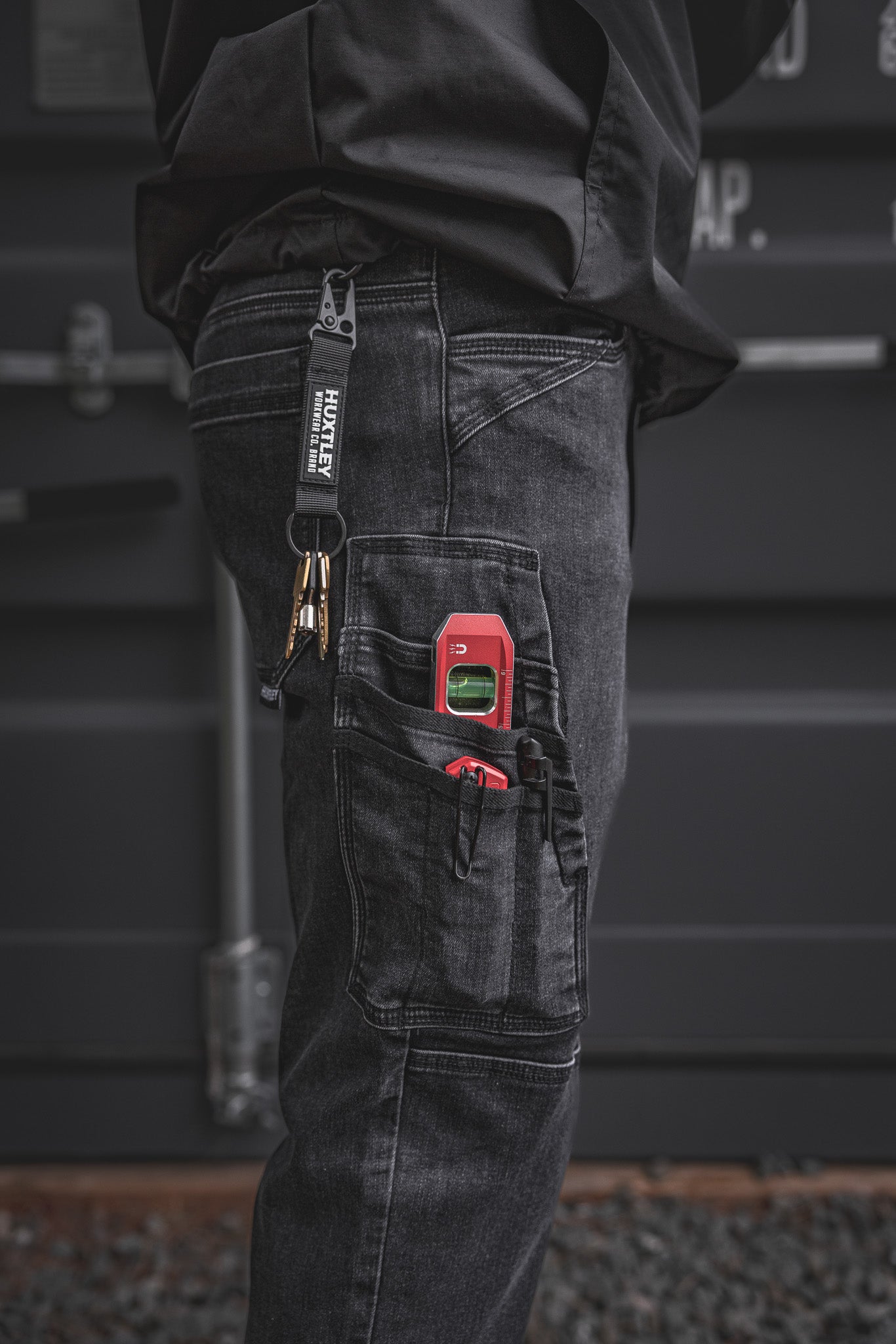 
                  
                    Close-up of the RX-1 Relaxed Work Jeans in Stonewashed Black showing off the side tool pocket and Huxtley-branded key clip. Built for trades with rugged stretch denim and jobsite-ready storage.
                  
                