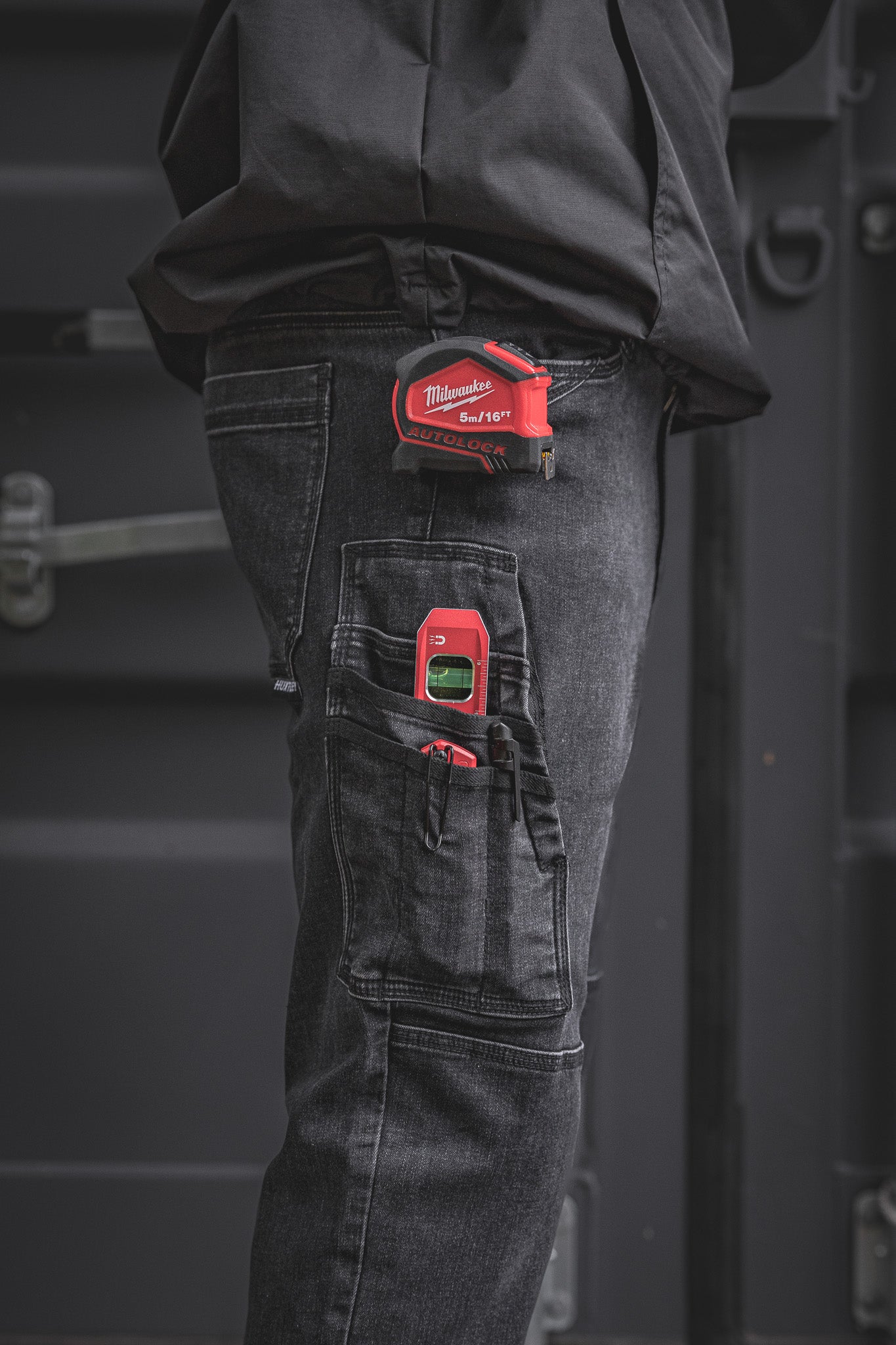 
                  
                    The RX-1 Relaxed Work Jeans in Stonewashed Black shown with a tape measure, laser level, and utility knife stored in the tool pocket. Built for practical on-site use and pro-level convenience.
                  
                